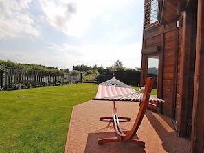 A wooden building with a hammock and a chair outside, a grassy yard, and a wooden fence.