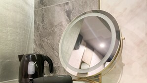 Une salle de bain avec un mur en marbre, une bouilloire électrique noire, un miroir compact avec un cadre doré et un lisseur noir.