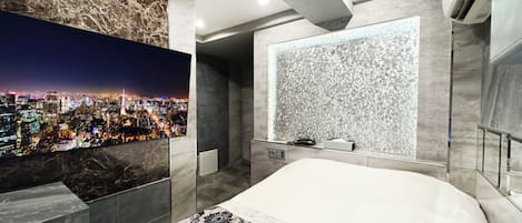 A modern hotel room with a cityscape view, a large bed, and a unique textured wall.