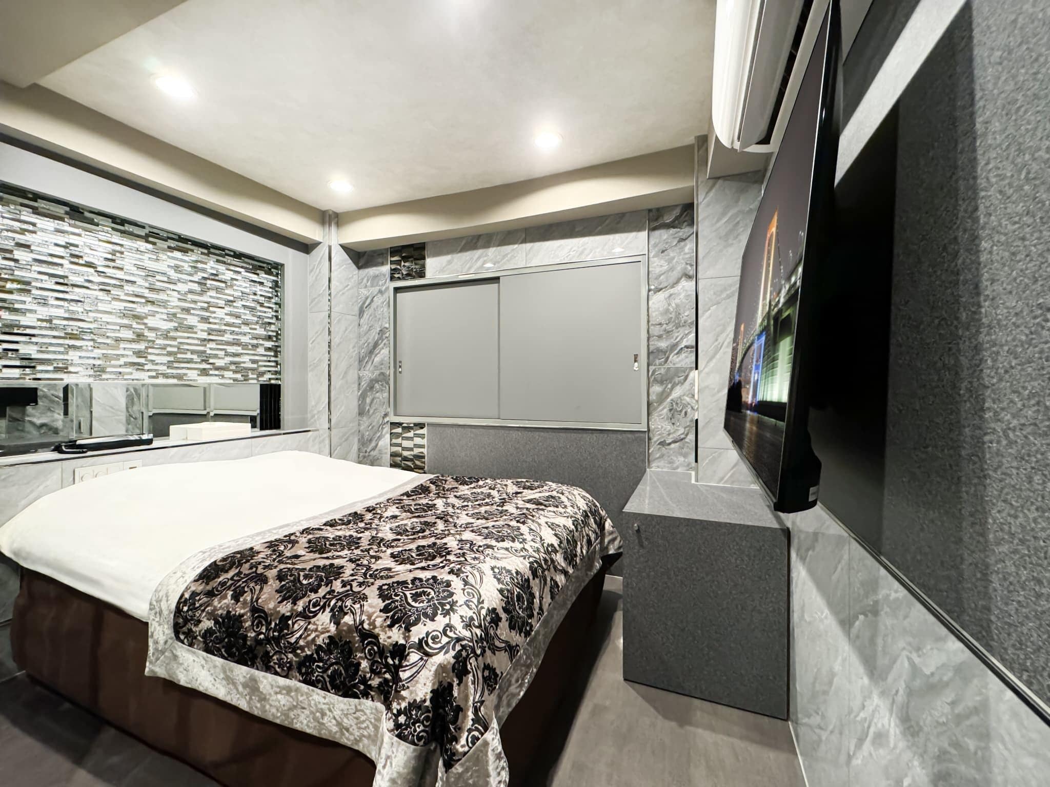 A modern bedroom with a large bed, a built-in wardrobe, and a flat-screen TV mounted on the wall.
