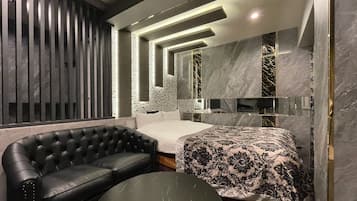 A modern bedroom with a black leather sofa, a round coffee table, a bed with a patterned bedspread, and a large mirror.