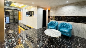 A lobby with a marble floor, two blue leather armchairs, a round table, and a reception desk. - Hotel Rocks (Tokyo)