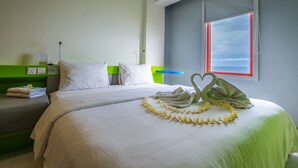 Una cama bien hecha con un cabecero blanco y verde, un lei con forma de corazón y una ventana con marco rojo.