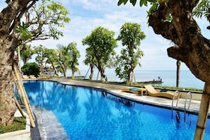 Una piscina azul cristalina rodeada de palmeras y sillas de descanso, con vista al mar.