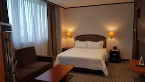 A hotel room with a bed, two bedside lamps, a nightstand, a desk, a chair, and a TV. - Abdul Razak Hotel Apartment (Bandar Seri Begawan)
