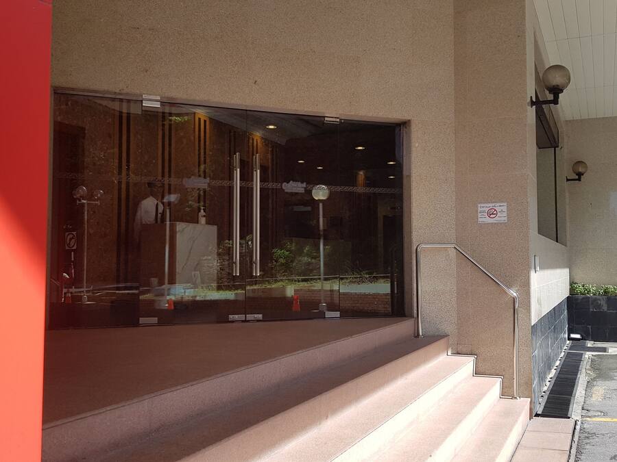 A hotel entrance with a glass door, steps leading up to it, and a no-smoking sign on the wall.