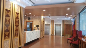 A hotel lobby with a reception desk, elevators, and red chairs. - Abdul Razak Hotel Apartment (Bandar Seri Begawan)
