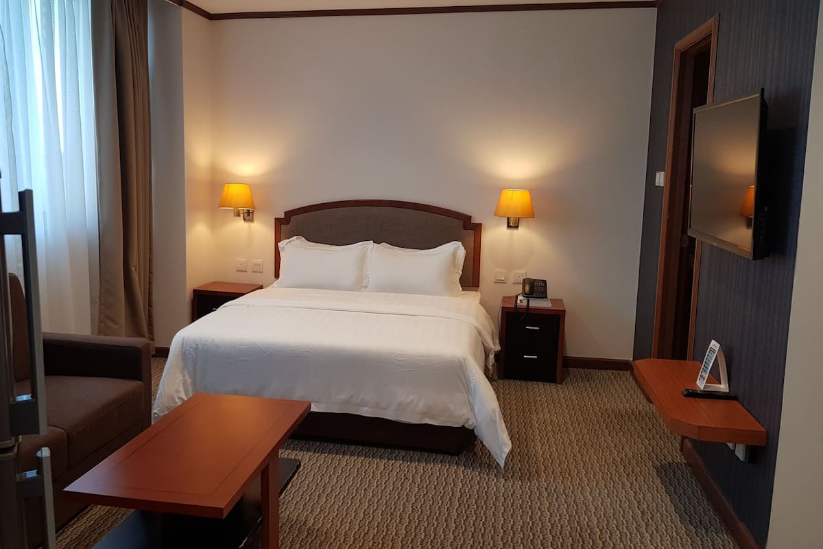 A hotel room with a bed, two bedside tables, a desk, a chair, and a TV mounted on the wall.