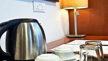 Quarto de hotel com uma secretária de madeira, chaleira, duas chávenas brancas, jarra de vidro e uma lâmpada.