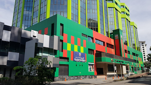 A modern building with a green and red facade, large windows, and a sign indicating it is a business center. - Abdul Razak Hotel Apartment (Bandar Seri Begawan)