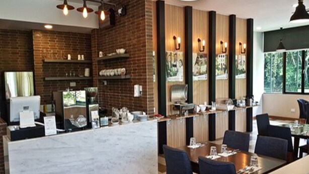 A modern restaurant with a brick wall, a long counter, and a dining area with tables and chairs. - Abdul Razak Hotel Apartment (Bandar Seri Begawan)