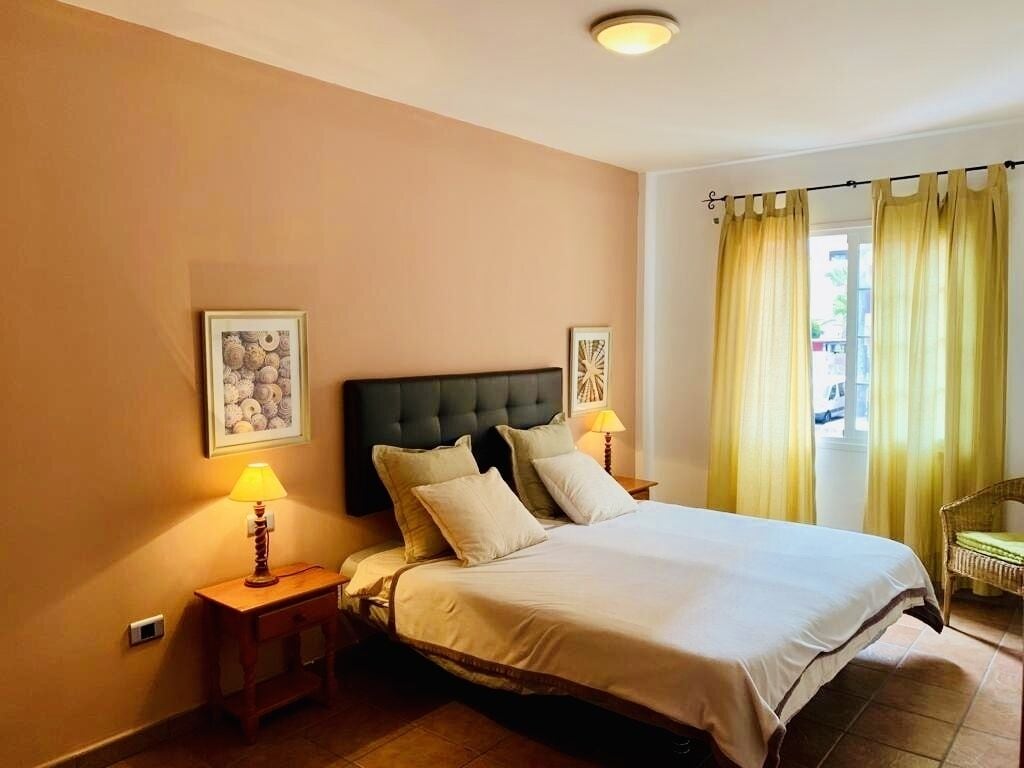 A hotel room with a large bed, two bedside lamps, a framed picture on the wall, and a window with yellow curtains.