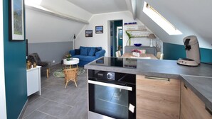Una cocina moderna con horno empotrado, un comedor con mesa y sillas, un sofá azul y una mesita auxiliar con un florero.