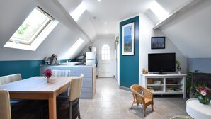 Un loft moderno con cocina, comedor y sala de estar. Cuenta con tragaluces, un televisor grande y una estantería.