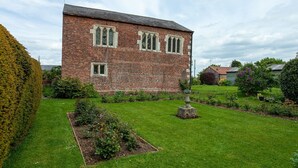Ein Backsteinhaus mit symmetrischer Fassade, einem zentralen Eingang und einem gepflegten Garten mit verschiedenen Pflanzen und einem Steinelement.