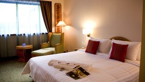 A hotel room with a large bed, a chair, a nightstand, a lamp, and a window with curtains. - The Centrepoint Hotel (Bandar Seri Begawan)