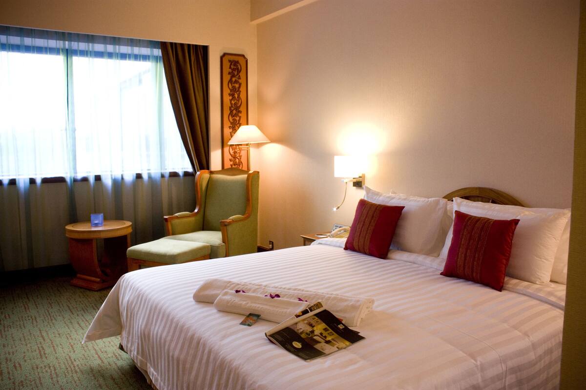 A hotel room with a large bed, a chair, a nightstand, a lamp, and a window with curtains.