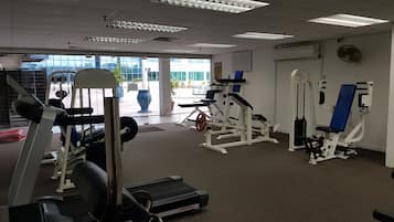 A gym with various exercise equipment, a treadmill, and a view of the outside through large windows.