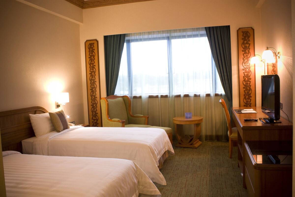 A hotel room with two beds, a desk with a computer, a chair, and a small table.