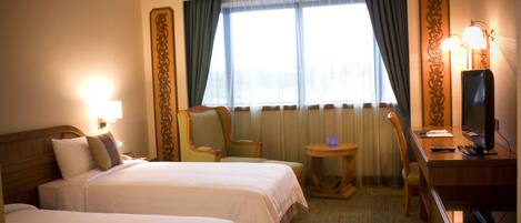 A hotel room with two beds, a desk with a computer, a chair, and a small table.
