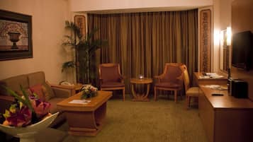 A hotel room with a sofa, two armchairs, a small table, a TV, and a large window with curtains.