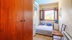 A bedroom with a wooden wardrobe, a bed with patterned bedding, a bedside table, and a window with curtains. - Club Villamar - Nice villa with airco, wifi, fenced private swimming pool nearby Calonge (Calonge)