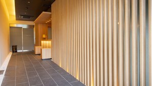 A modern hotel corridor with a wooden slatted wall, a reception desk, and a guest room door. - First Cabin Kyoto Nijojo (Kyoto)