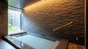 A modern bathroom with a glass shower enclosure, a stone wall, and a metal handrail. - First Cabin Kyoto Nijojo (Kyoto)