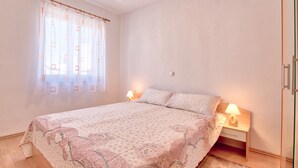 A bedroom with a bed, two bedside lamps, a window with curtains, and a wooden nightstand.