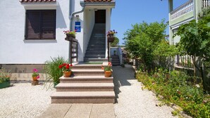 A building with a staircase leading to a door, surrounded by potted plants and a gravel path.