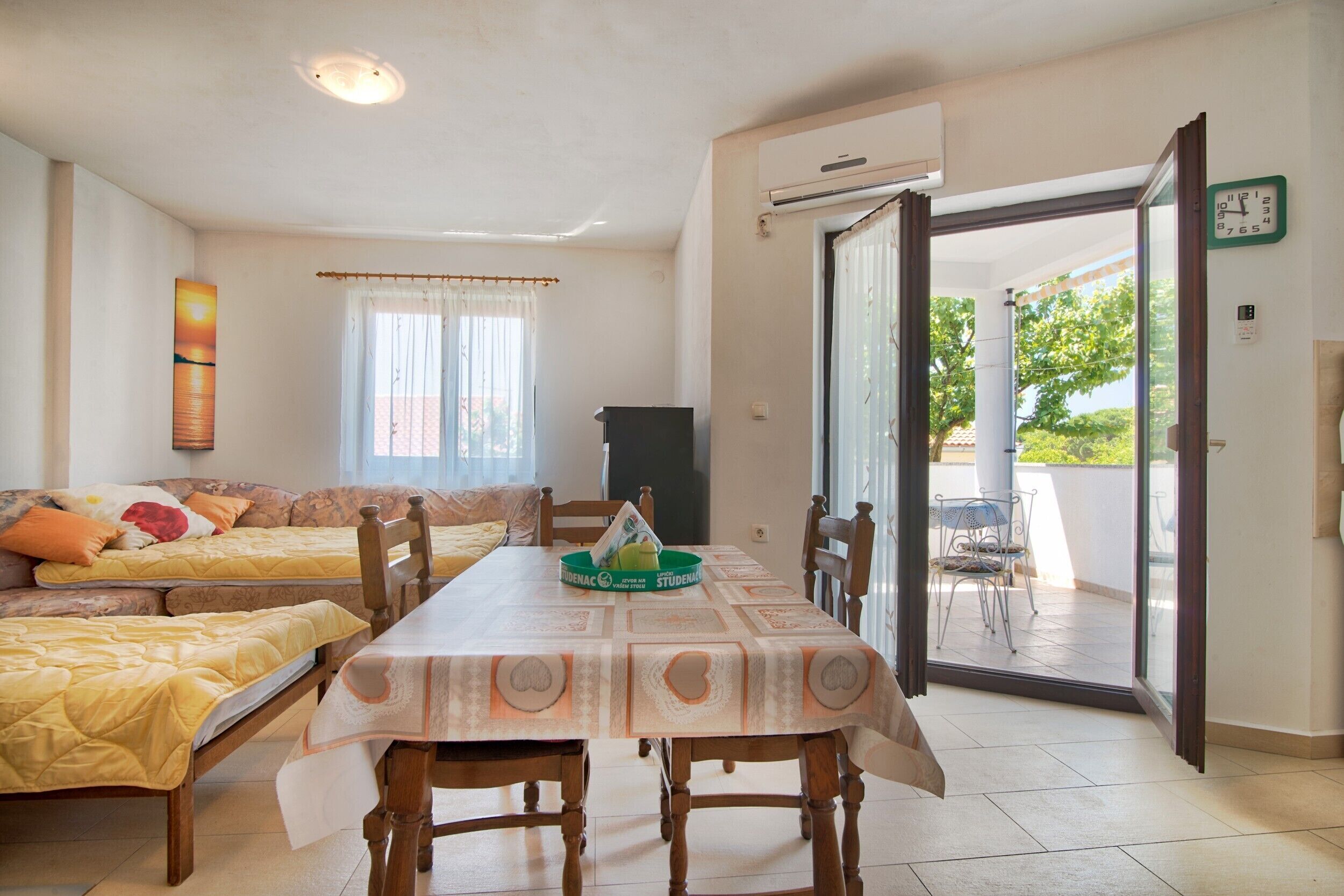 Una habitación con una mesa de comedor, dos camas, un sofá y un ventanal corredizo que da a un espacio exterior.