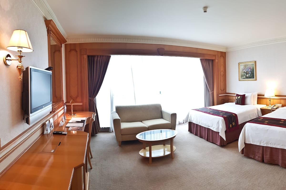 Ein Hotelzimmer mit zwei Betten, einem Sofa, einem Fernseher, einem Schreibtisch und einem kleinen Tisch.