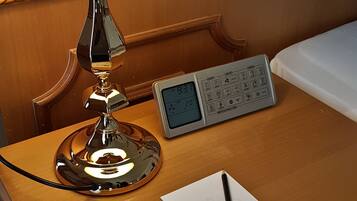 A wooden nightstand with a white lamp, a digital clock, a notepad, and a pen.