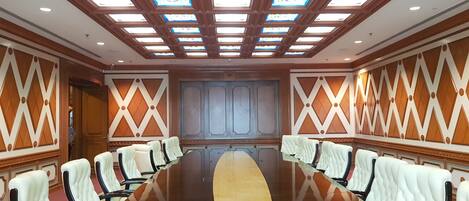 A conference room with a long table, white leather chairs, wooden paneling, and a high ceiling with skylights.
