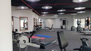 Un gimnasio con máquinas de cardio, equipo de levantamiento de pesas y espejos en las paredes.