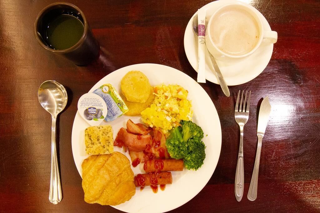 Une assiette remplie de plats pour le petit-déjeuner, comprenant des œufs, du bacon, des saucisses et des légumes, accompagnée d’une tasse de café et de couverts, le tout posé sur une table en bois.