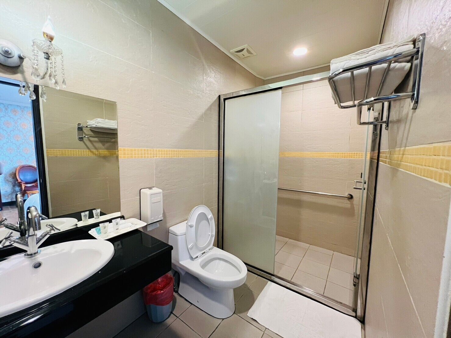 A modern bathroom with two sinks, a toilet, a glass shower enclosure, and a chandelier.