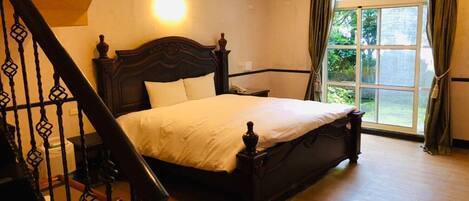 Un dormitorio con una cama grande, un cabecero de madera, una mesita de noche, una silla y un ventanal con cortinas.