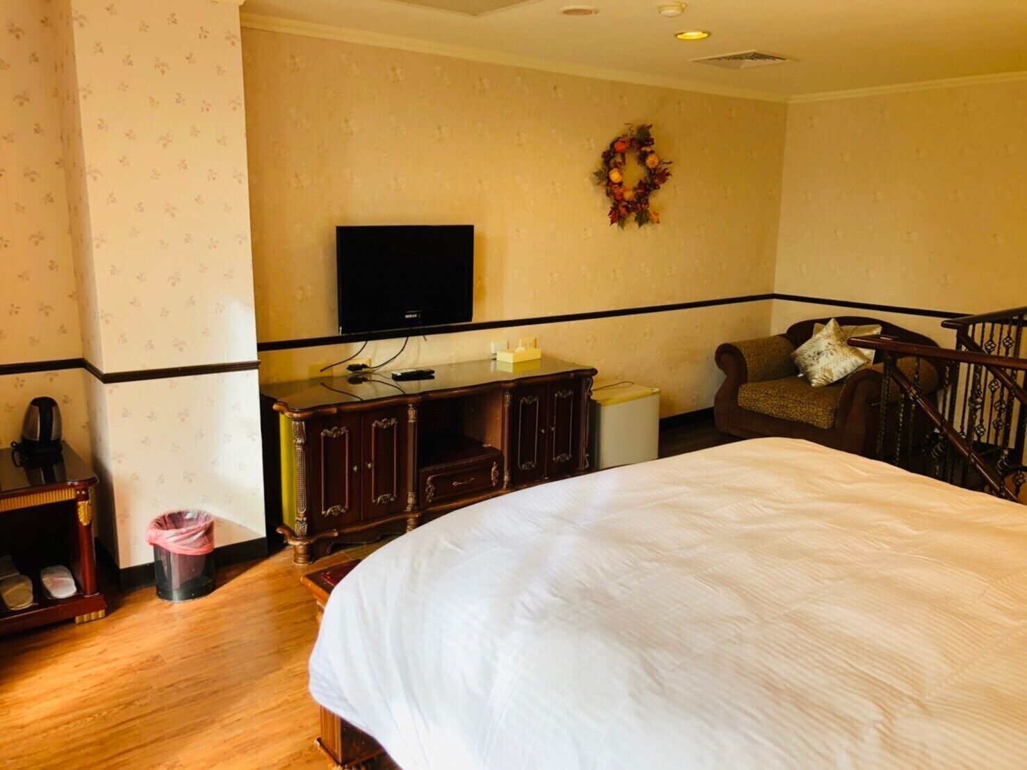 A hotel room with a bed, a television, a dresser, a chair, and a small trash bin.