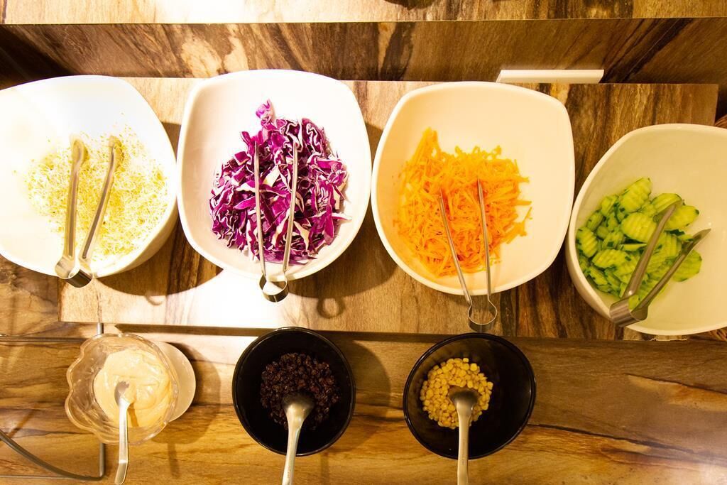 A wooden table with five white bowls containing different food items and two black bowls with sauces.