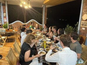 A group of people dining at an outdoor table with a brick wall and large windows in the background.