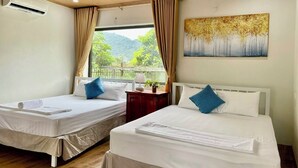 A hotel room with two beds, a ceiling fan, an air conditioning unit, a painting, and a view of greenery outside. - Phong Nha An An Homestay (Phong Nha)