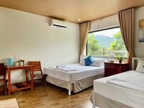 A hotel room with two beds, a wooden desk, a chair, a small table, an air conditioning unit, and a window with curtains. - Phong Nha An An Homestay (Phong Nha)