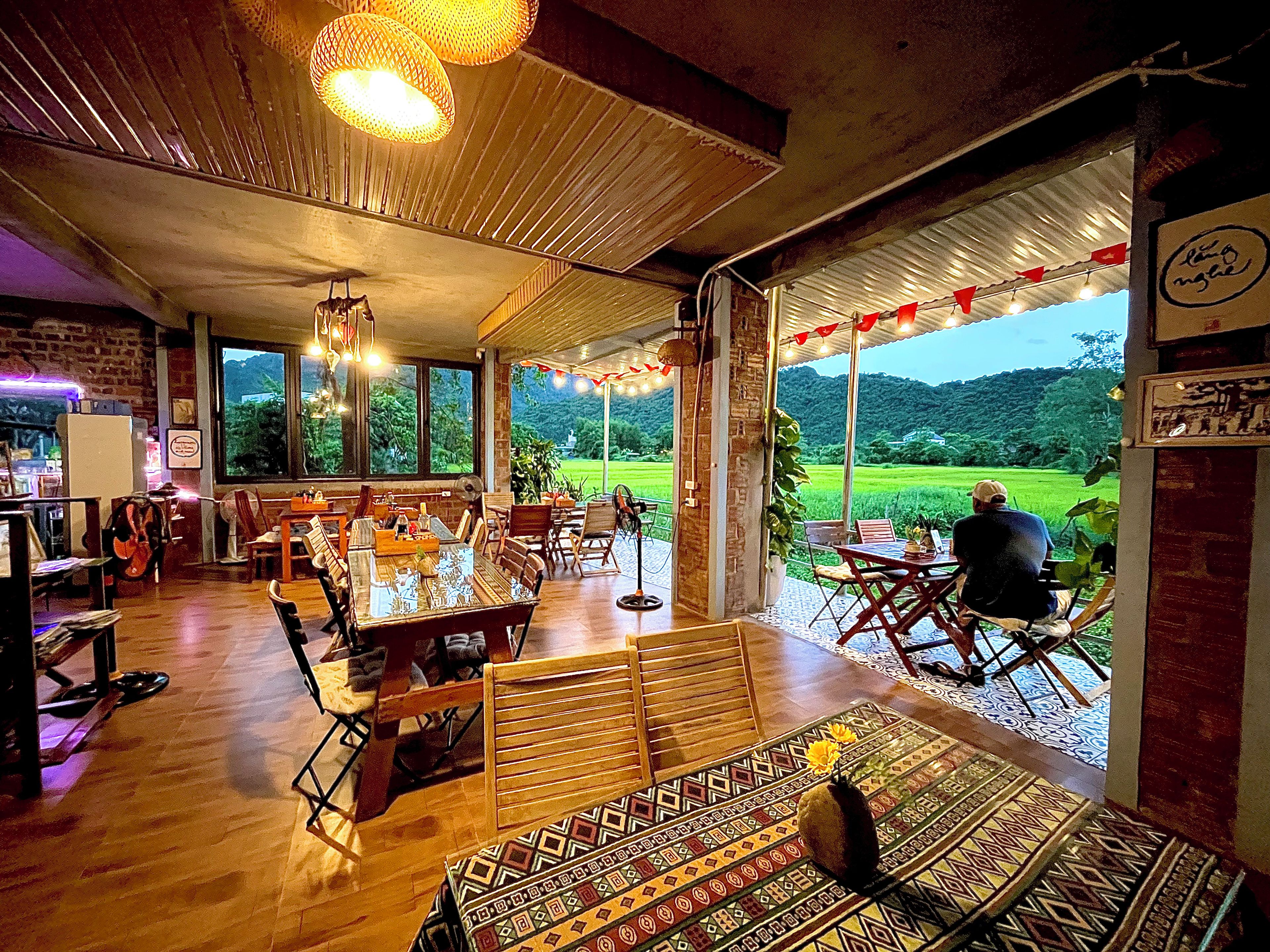 Un restaurante con vistas a un campo verde, muebles de madera y luces colgantes.