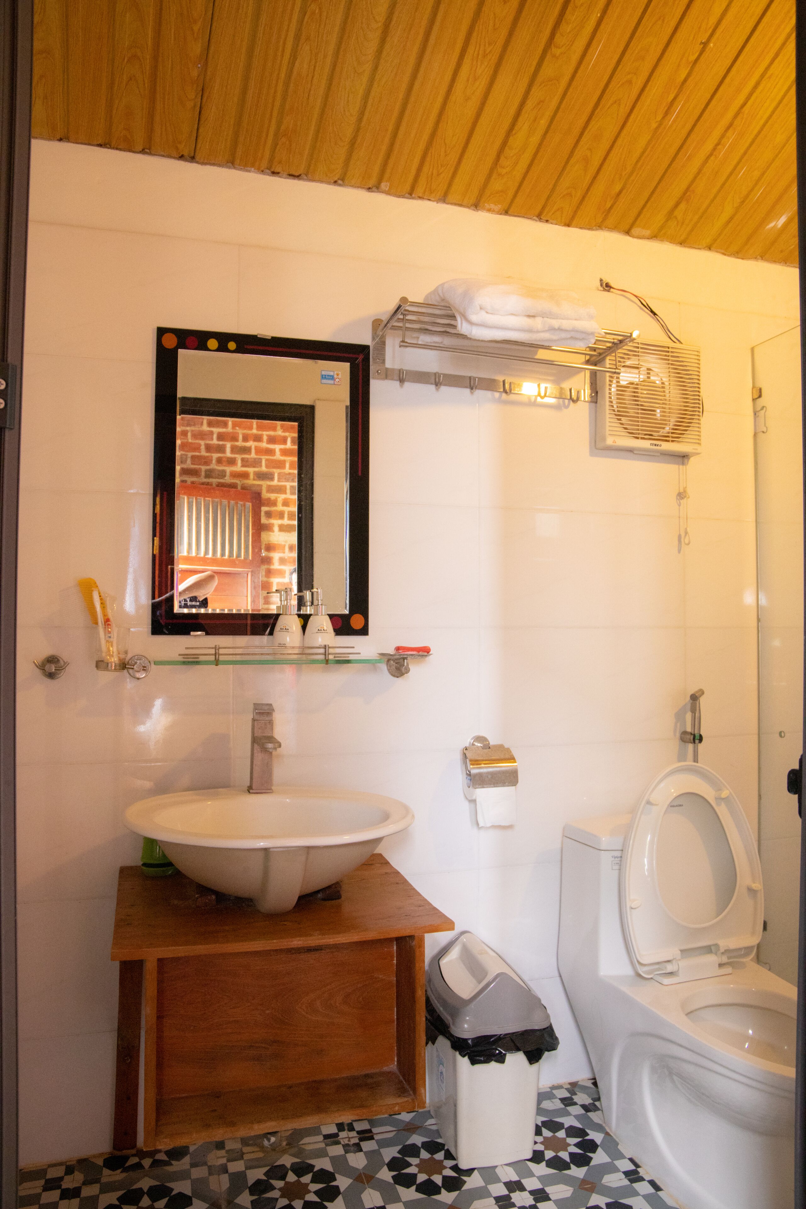 Un baño con tocador de madera, un lavamanos blanco, un espejo, un inodoro y un cubo de basura.