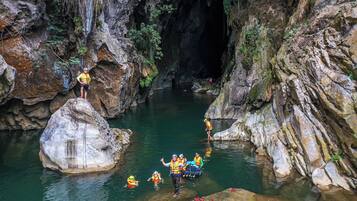 A group of people in a rocky canyon with a river, some standing on rocks and others in the water.