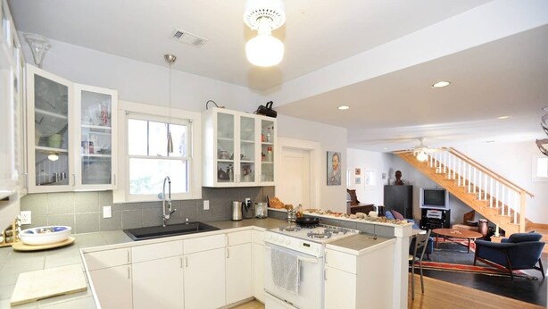 A modern kitchen with white cabinetry, a built-in oven, and a large island with a sink. - Cool Updated Craftsman Bungalow (Austin)