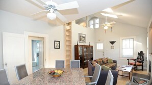 A spacious living room with a large dining table, a fireplace, and a high ceiling with ceiling fans. - Cool Updated Craftsman Bungalow (Austin)
