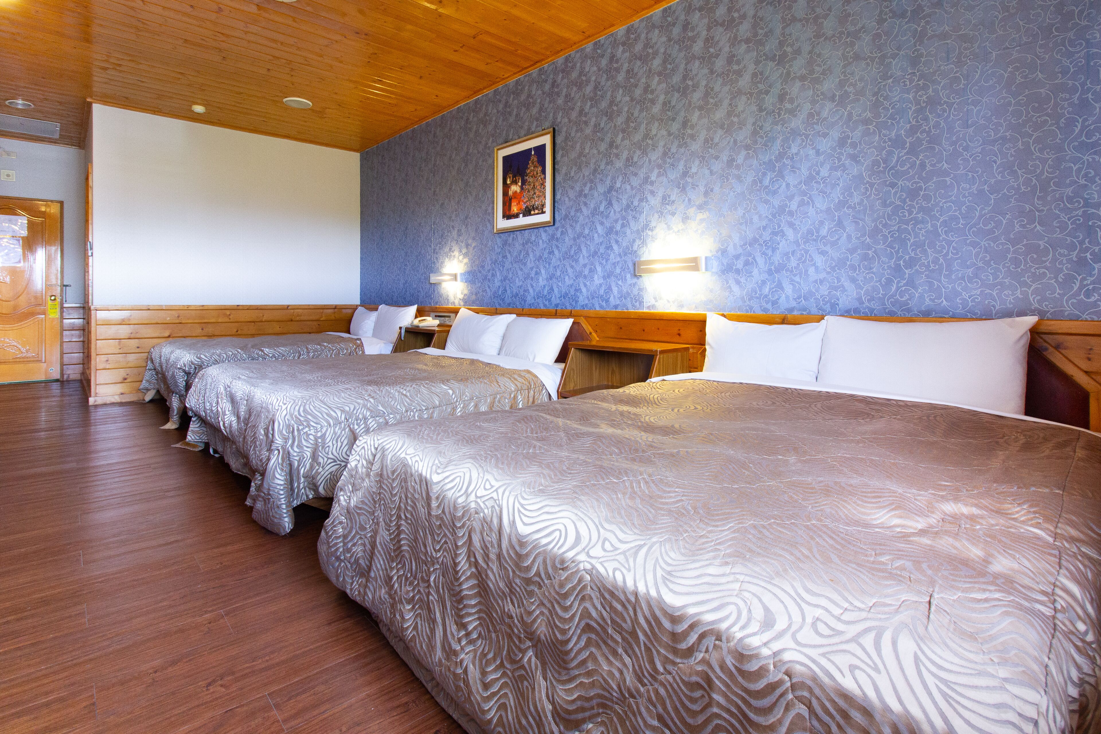 A hotel room with two beds, wooden flooring, and a blue patterned wall.