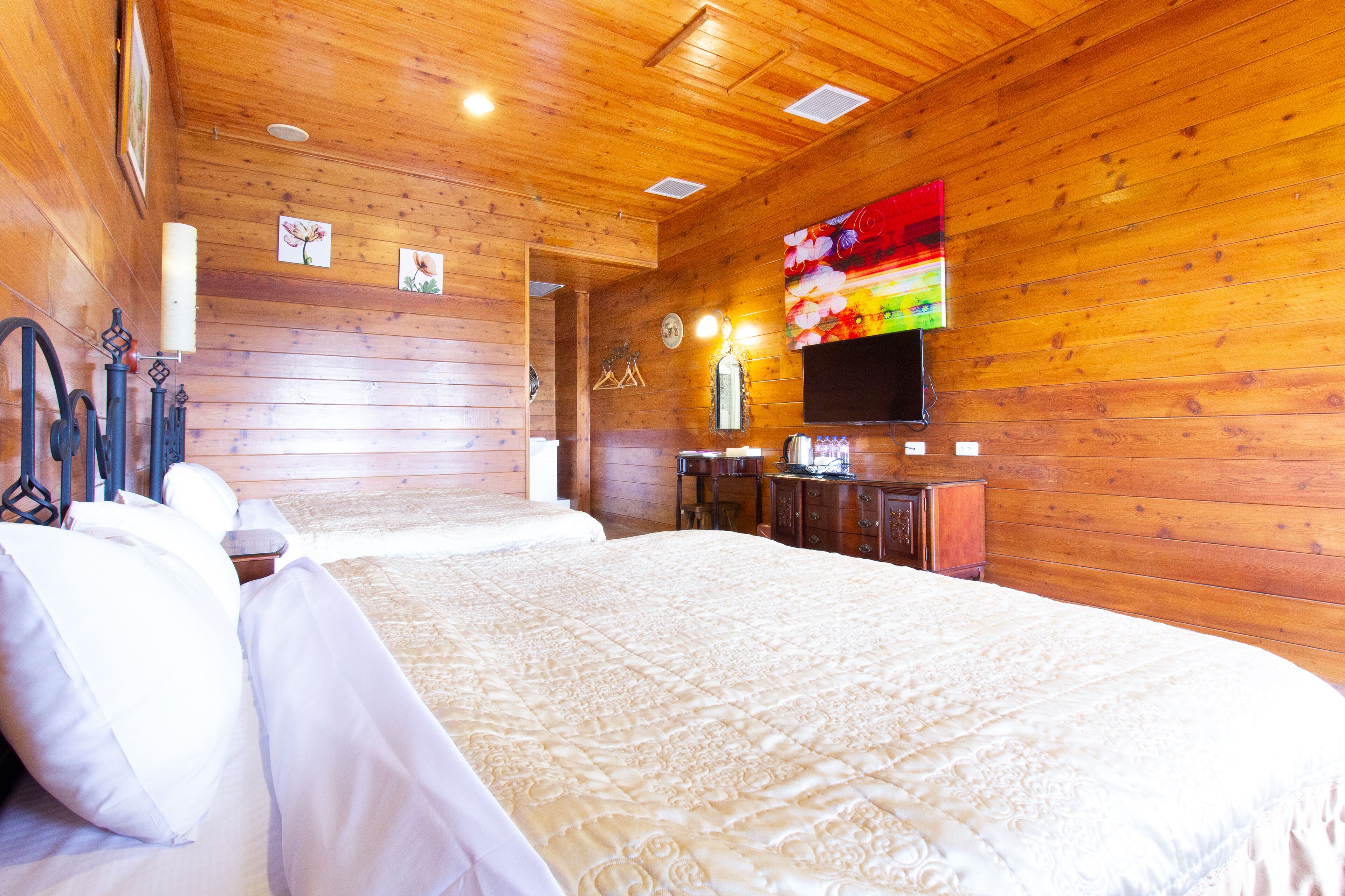 A wooden-paneled room with a large bed, a flat-screen TV mounted on the wall, and a wooden dresser.